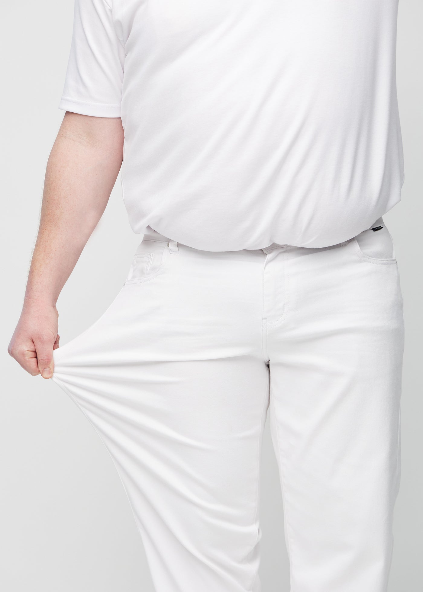 Plus-size model strækker jeansene ved låret for at vise stretch.