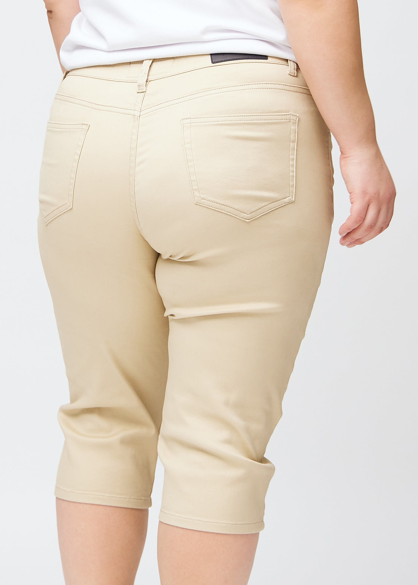 Tæt billede af bagdelen på en plus-size model i beige slim capris – detaljefokus på lommer og syninger.