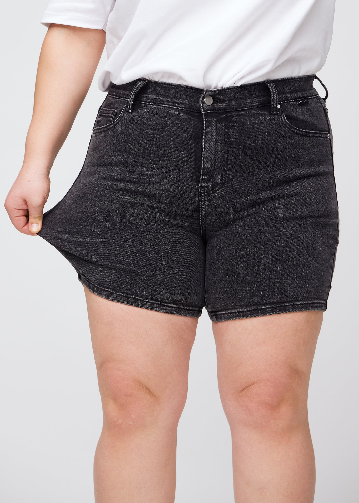 Plus-size model strækker shortsene ved låret for at vise stretch.