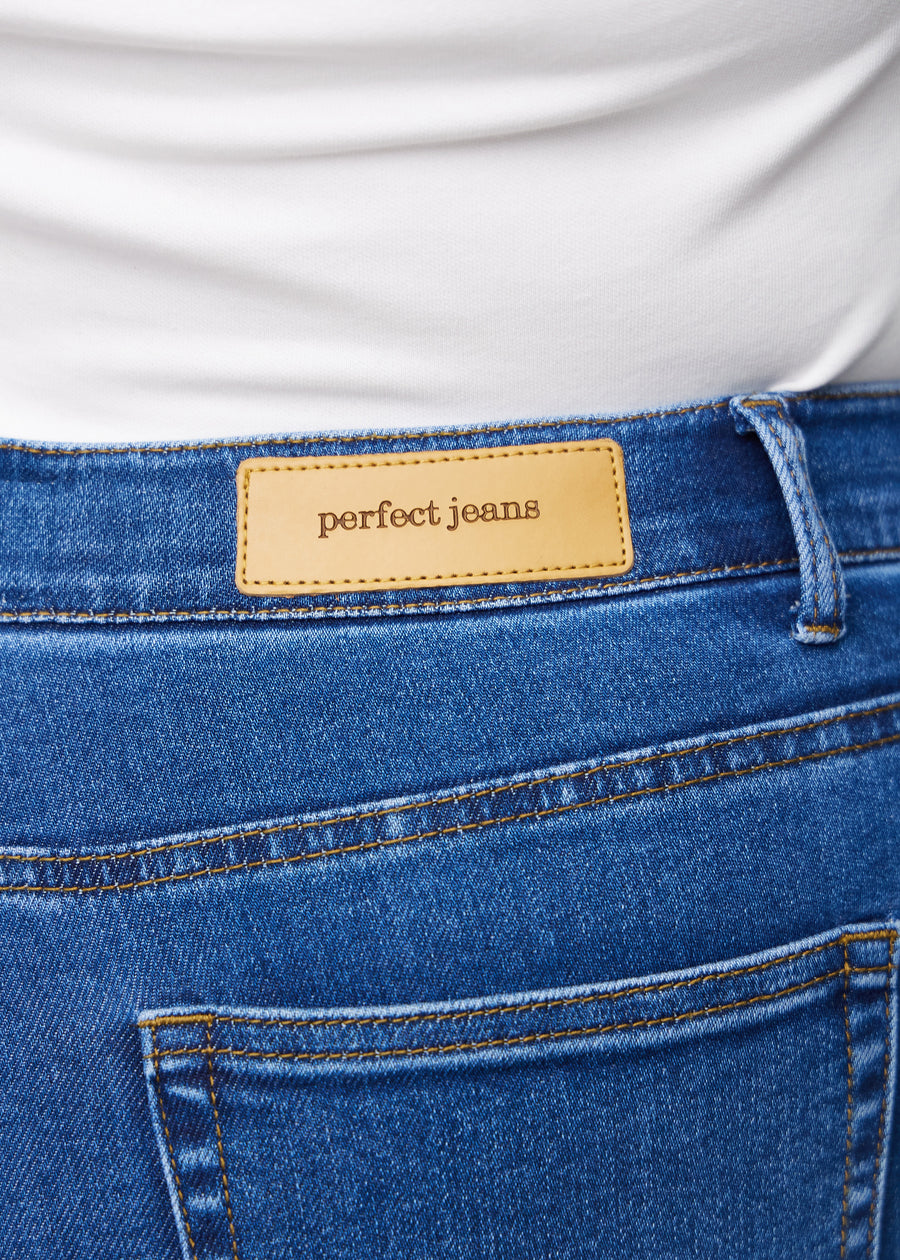 Nærbilde av mørkeblå denim med Perfect Jeans lærpatch bak i linningen på en plus-size modell.