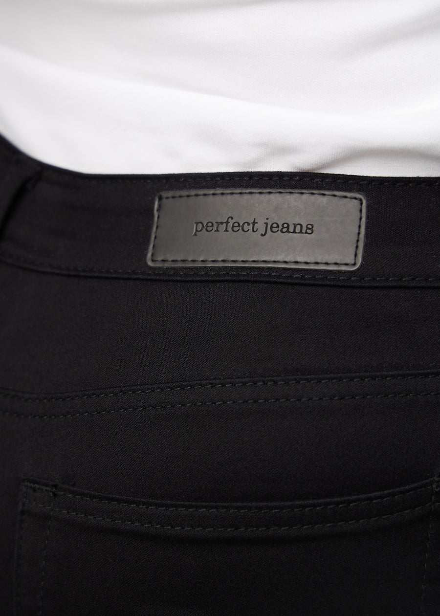 Nærbilde av sort jeansmateriale med Perfect Jeans-logoetikett ved kanten av forlommen på en plus-size modell.