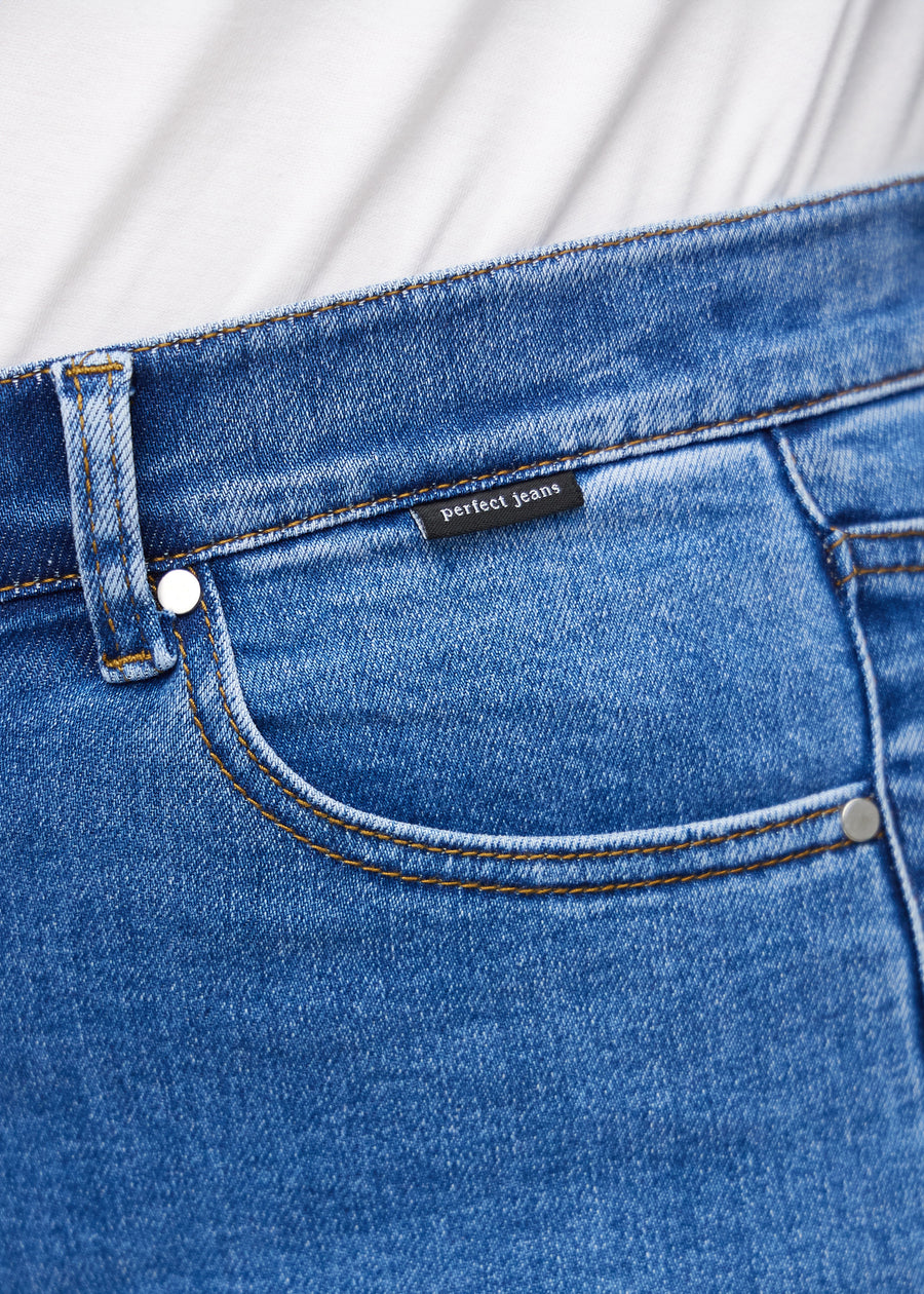 Nærbilde av blå denim med Perfect Jeans-logoetikett ved kanten av forlommen på en plus-size modell.