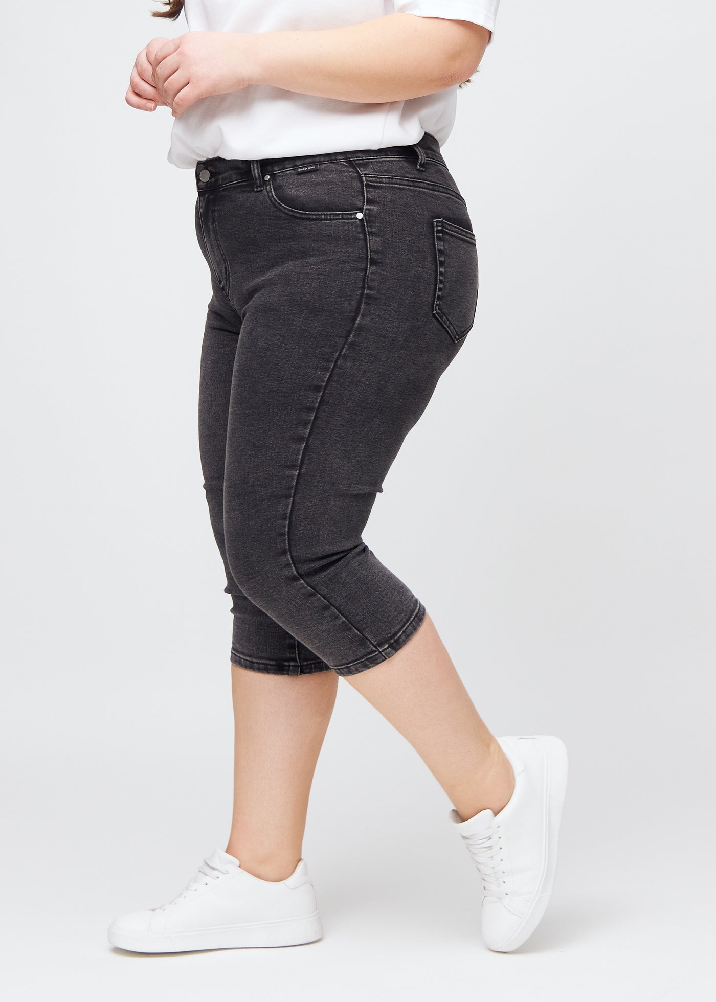 Mørkegrå denim skinny capris set fra siden på en plus-size model.