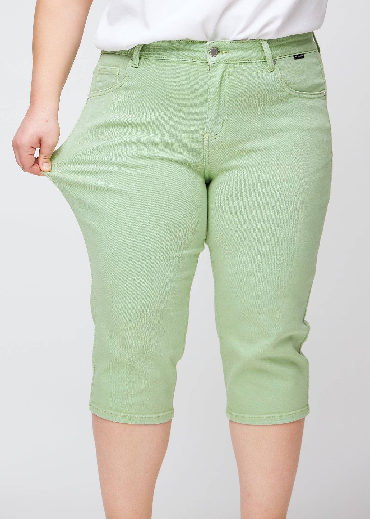 Plus-size model viser stretch ved at trække i caprisene ved låret – fokus på komfort og fleksibilitet.