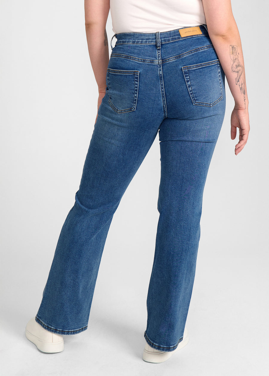 Mørkeblå denim bootcut jeans, modelnavn Oceans, som sidder tæt om hofter og lår med et let svaj fra knæet og ned, set bagfra, så man kan se hele produktet. på en plus-size model.