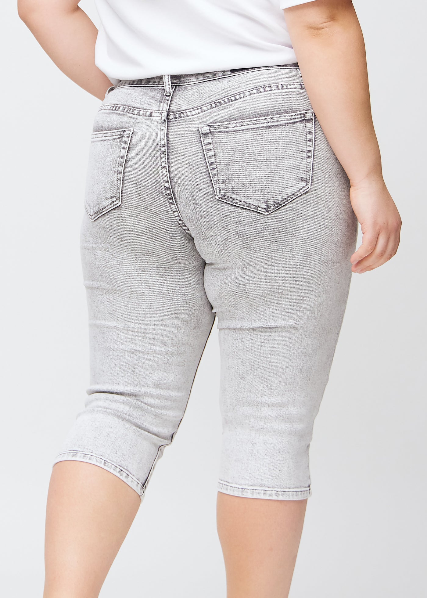 Tæt billede af bagdelen på en plus-size model i lysegrå denim slim capris – detaljefokus på lommer og syninger.
