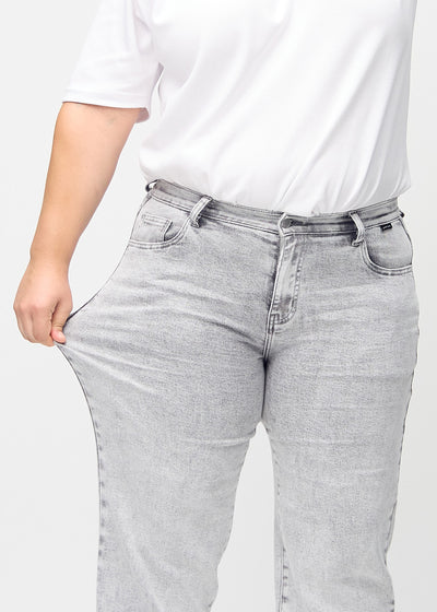 Plus-size model strækker jeansene ved låret for at vise stretch.