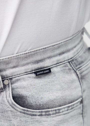 Nærbillede af lysegrå denim med Perfect Jeans logoetiket ved forlommekanten.