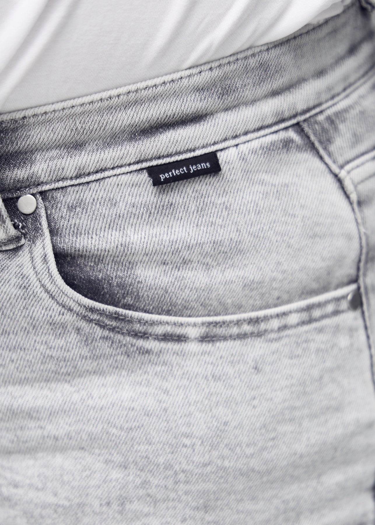 Nærbillede af lysegrå denim med Perfect Jeans logoetiket ved forlommekanten, på en plus-size model.