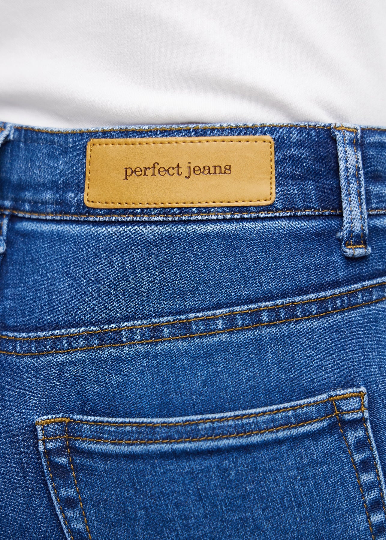 Nærbilde av mørkeblå denim med Perfect Jeans lærpatch bak i linningen.