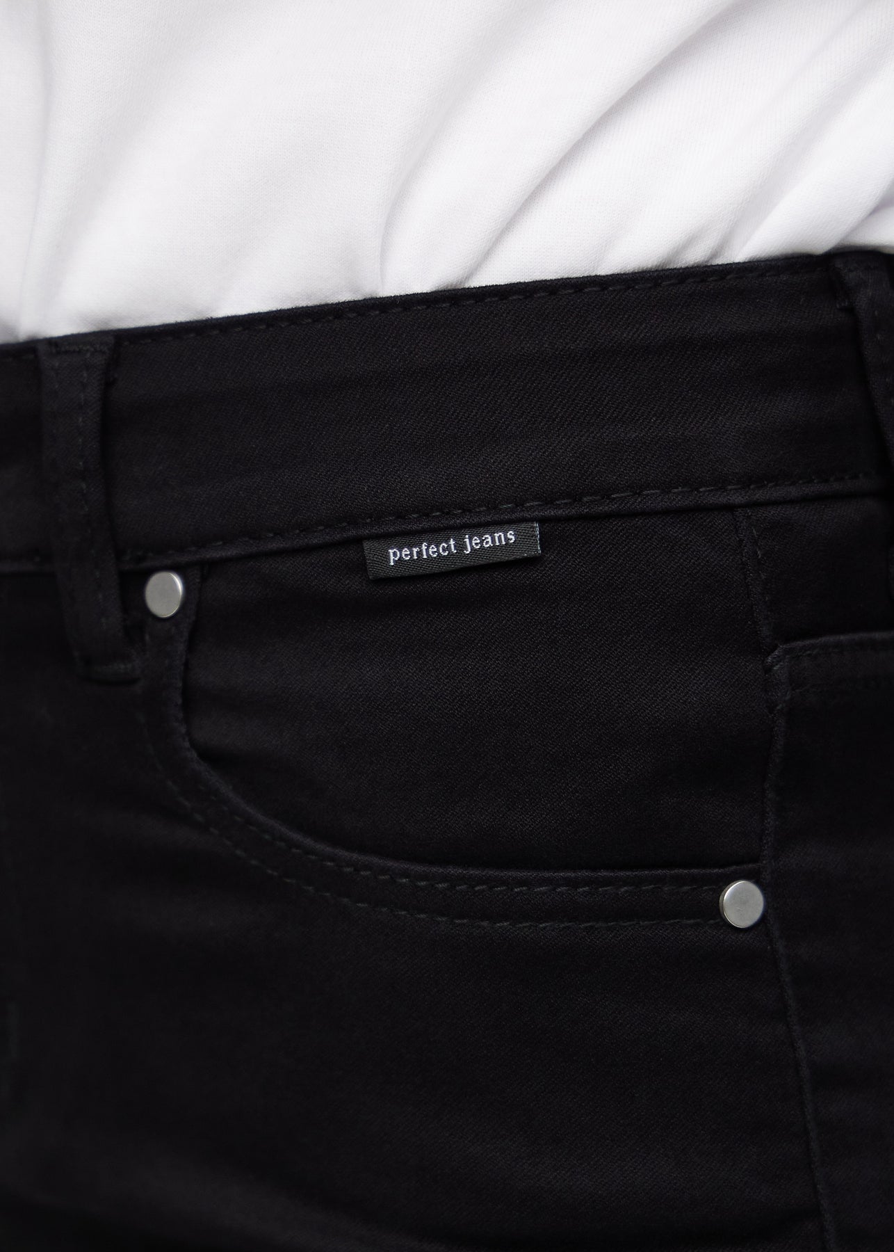 Nærbillede af sort jeansmateriale med Perfect Jeans logoetiket ved forlommekanten.