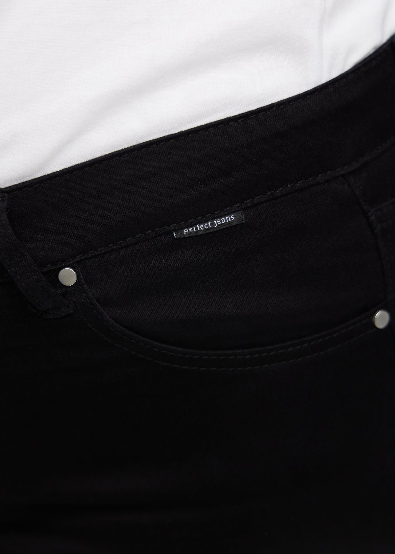 Nærbillede af sort jeansmateriale med Perfect Jeans logoetiket ved forlommekanten, på en plus-size model.