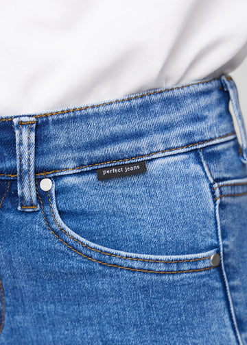 Nærbilde av blå denim med Perfect Jeans-logoetikett ved kanten av forlommen.