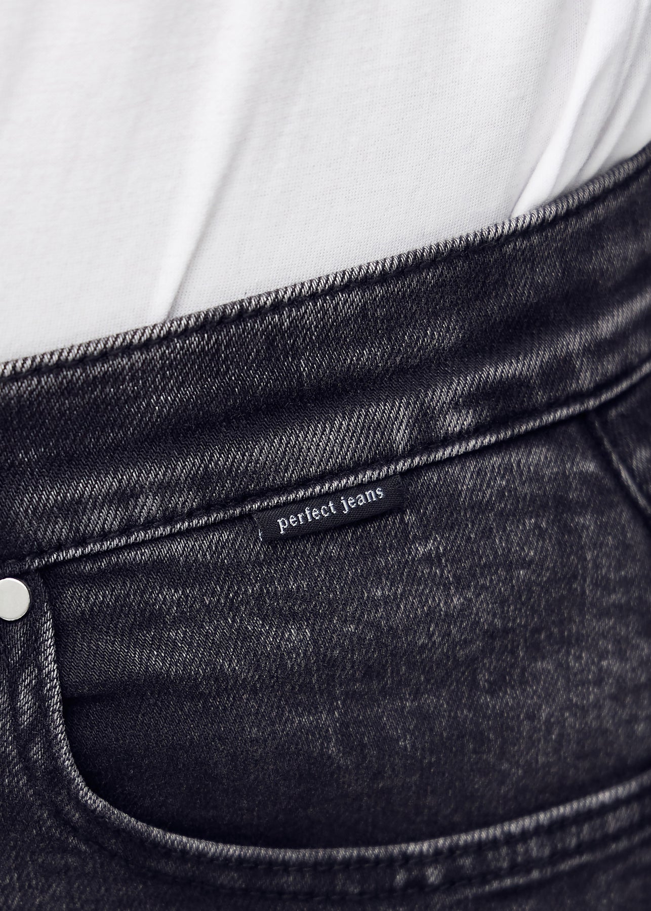 Nærbillede af mørkegrå denim med Perfect Jeans logoetiket ved forlommekanten.