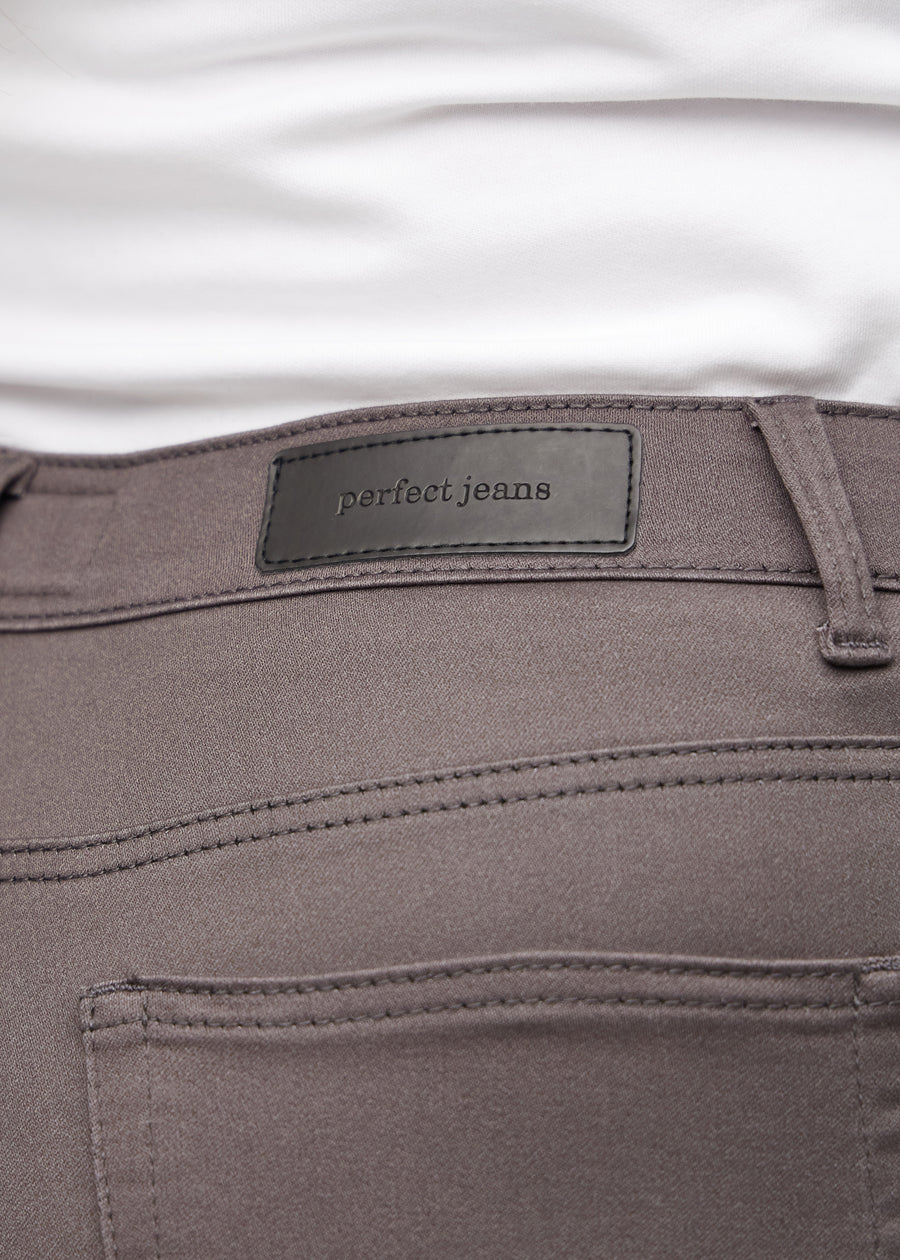 Nærbillede af gråbrunt jeansmateriale med Perfect Jeans læderpatch bagpå i taljen, på en plus-size model.