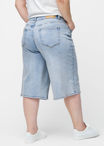 Løse, lyseblå denim capris i fargen Waves sett bakfra på plus-size modell, slik at passform og lengde kan sees.