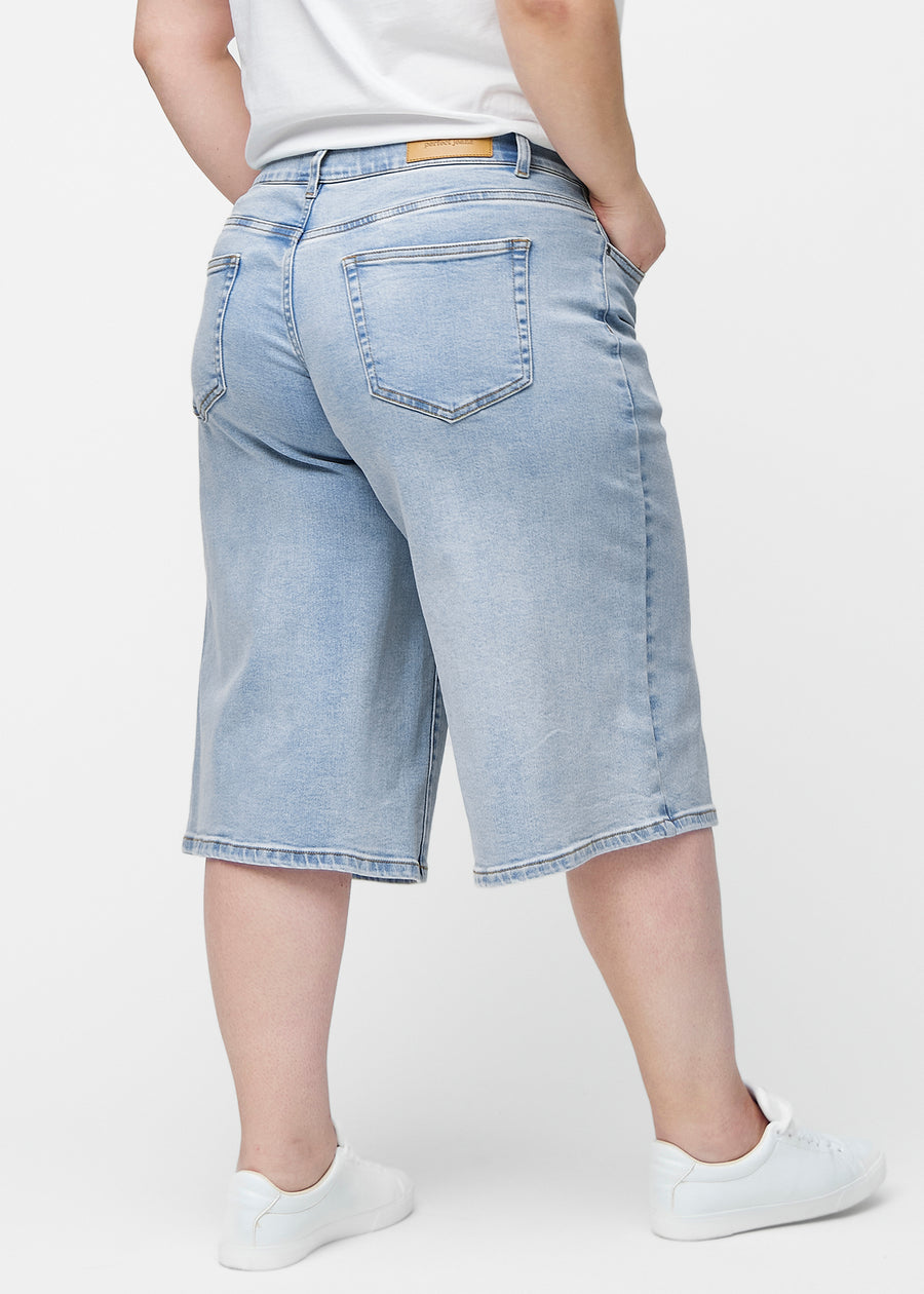 Løse, lyseblå denim capris i fargen Waves sett bakfra på plus-size modell, slik at passform og lengde kan sees.