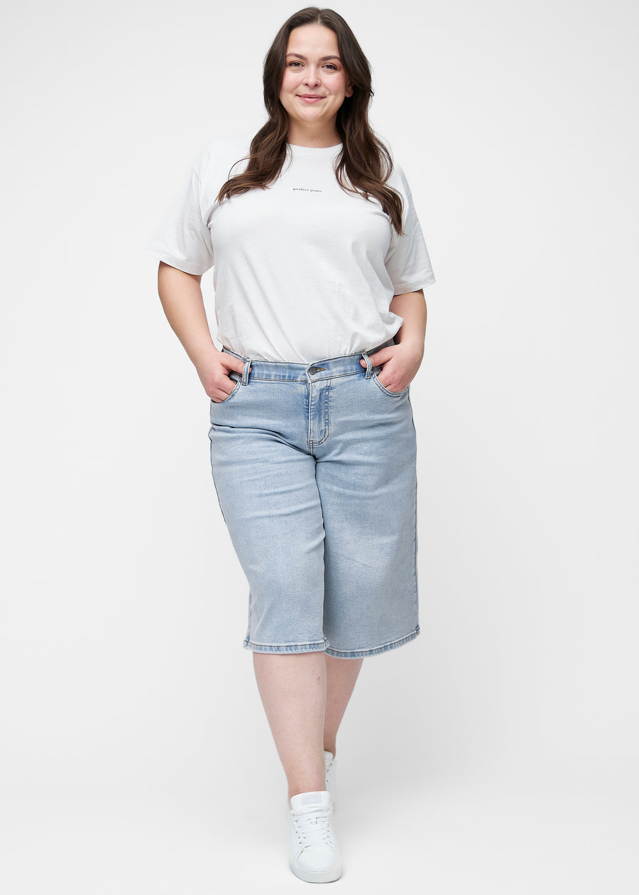 Fullt bilde av plus-size modell i løse, lyseblå denim capris i fargen Waves som går til rett under kneet.