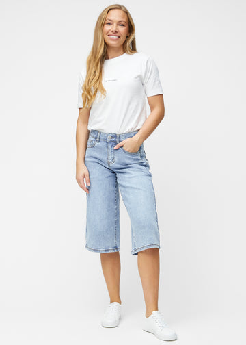 Fullt bilde av modell i løse, lyseblå denim capris i fargen Waves som går til rett under kneet.
