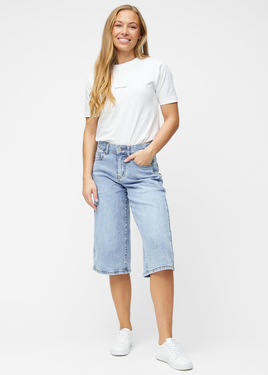 Fullt bilde av modell i løse, lyseblå denim capris i fargen Waves som går til rett under kneet.
