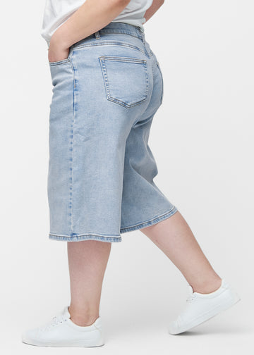Løse, lyseblå denim capris i fargen Waves sett fra siden på plus-size modell, hvor den brede passformen og lengden til rett under kneet er synlig.