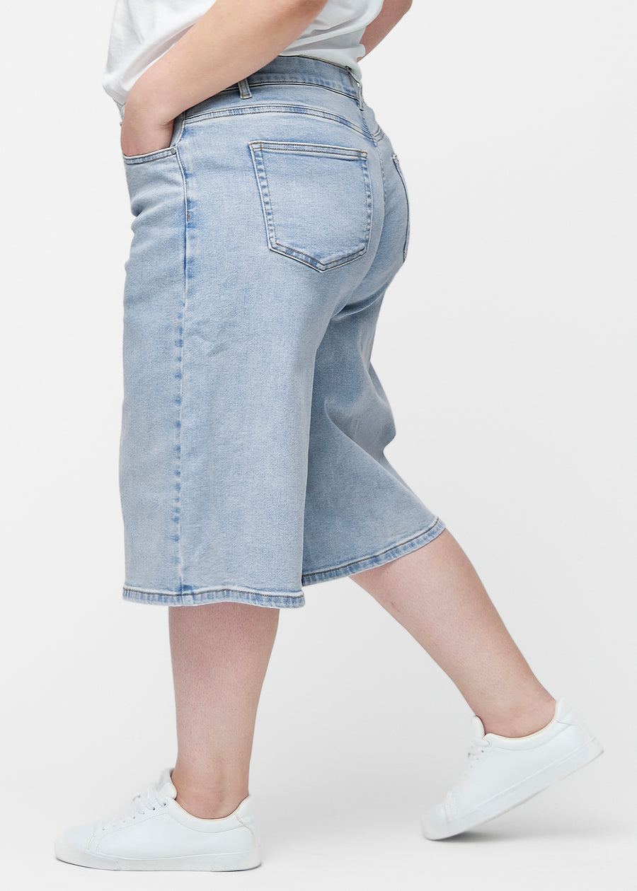 Løse, lyseblå denim capris i fargen Waves sett fra siden på plus-size modell, hvor den brede passformen og lengden til rett under kneet er synlig.
