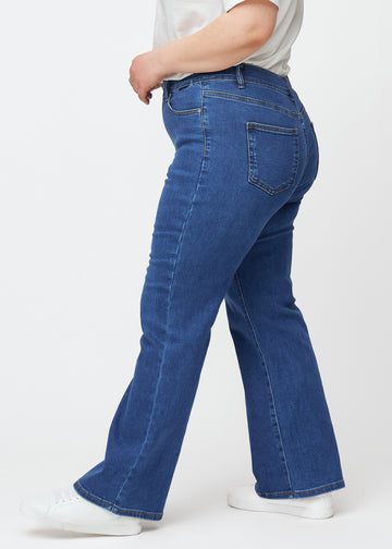 Mørkeblå mid-rise bootcut-jeans i fargen Oceans. Sett fra siden på en plus size-modell.