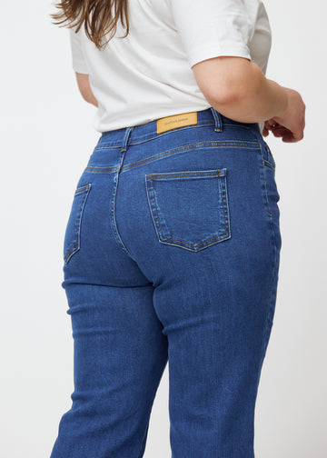 Mørkeblå mid-rise bootcut-jeans i fargen Oceans. Nærbilde bakfra på en plus size-modell for å vise detaljene.