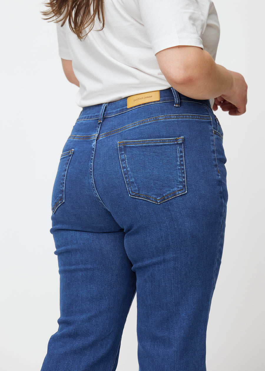 Mørkeblå mid-rise bootcut-jeans i fargen Oceans. Nærbilde bakfra på en plus size-modell for å vise detaljene.