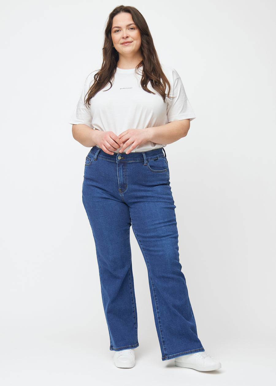 Mørkeblå mid-rise bootcut-jeans i fargen Oceans. Helhetsbilde av en plus size-modell med jeansene på.