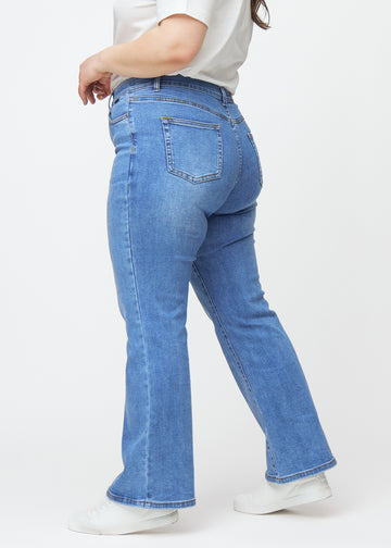 Blå mid-rise bootcut-jeans i fargen Rivers. Sett fra siden på en plus size-modell.
