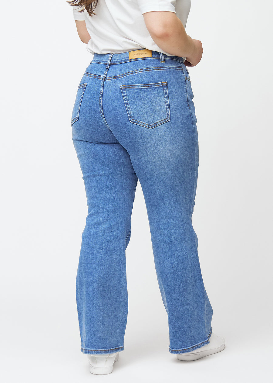 Blå mid-rise bootcut-jeans i fargen Rivers. Sett bakfra på en plus size-modell, slik at hele passformen vises.