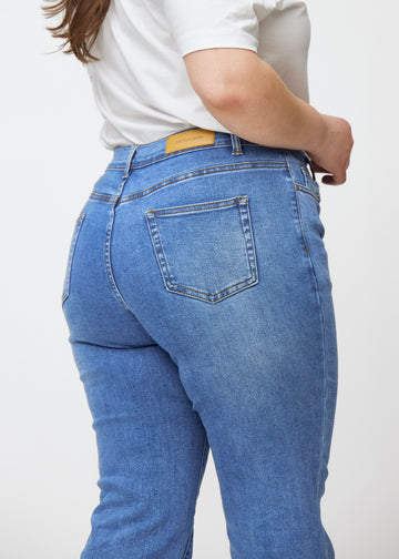 Blå mid-rise bootcut-jeans i fargen Rivers. Nærbilde bakfra på en plus size-modell for å vise detaljene.