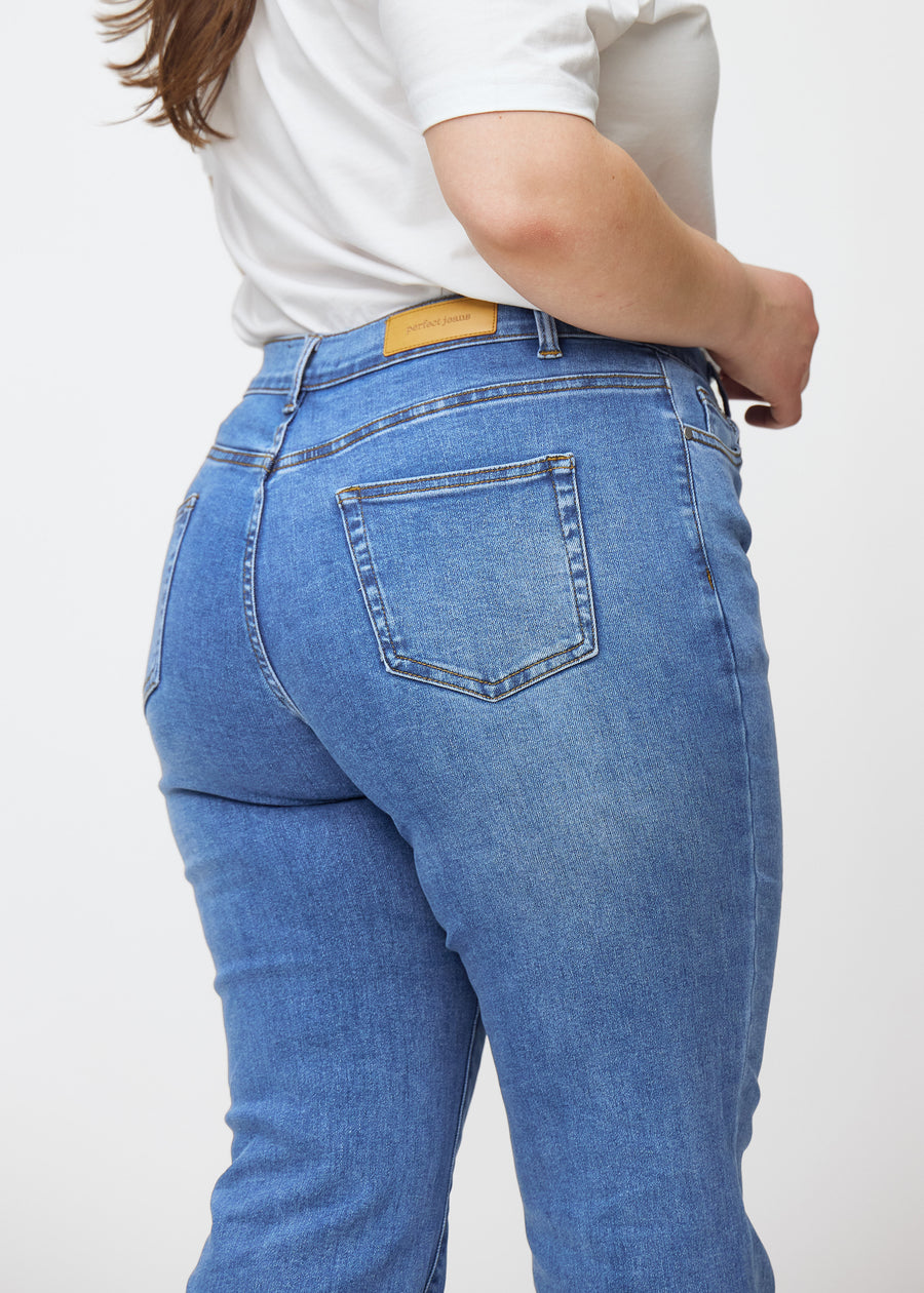 Blå mid-rise bootcut-jeans i fargen Rivers. Nærbilde bakfra på en plus size-modell for å vise detaljene.
