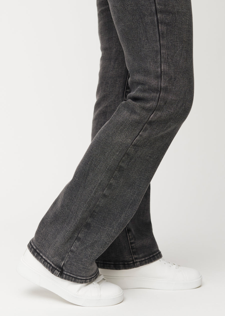 Mørkegrå mid-rise bootcut-jeans i fargen Shadows. Nærbilde ved ankelen på en modell som viser den lette utsvingen nederst.