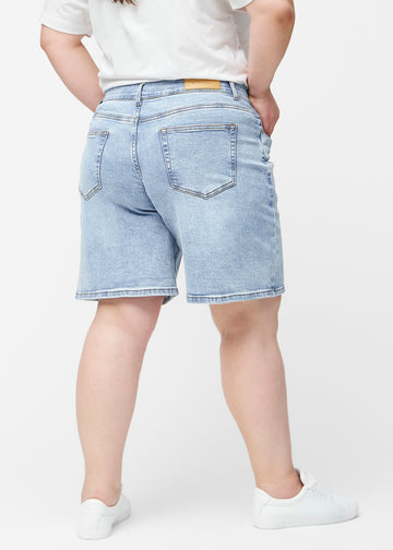 Løse, lyseblå denimshorts i fargen Waves sett fra siden på plus-size modell, hvor den brede passformen og lengden til rett over kneet er synlig.