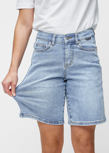 Løse, lyseblå denimshorts i fargen Waves som sitter ved hoften og faller løst ned over lårene til rett over kneet, sett forfra.