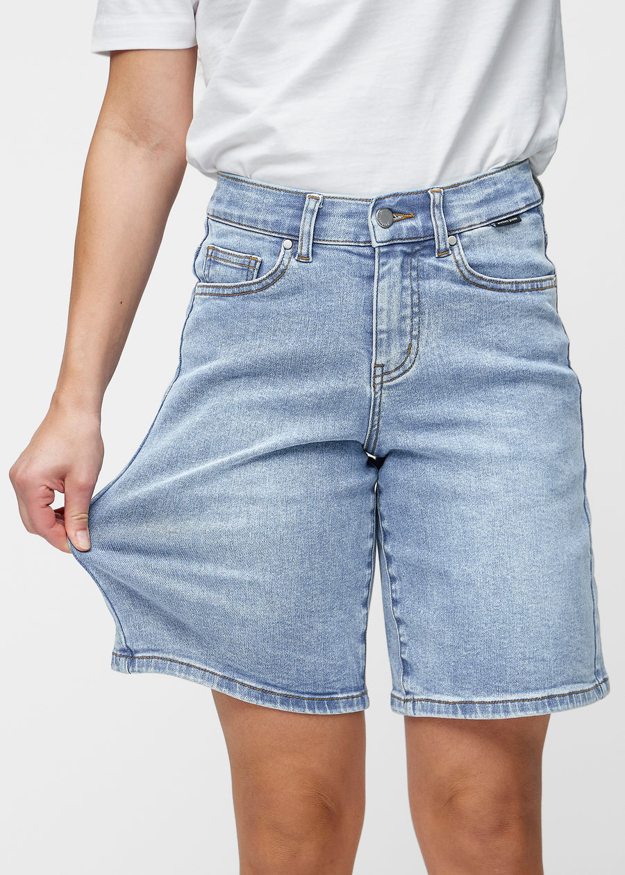 Løse, lyseblå denimshorts i fargen Waves som sitter ved hoften og faller løst ned over lårene til rett over kneet, sett forfra.