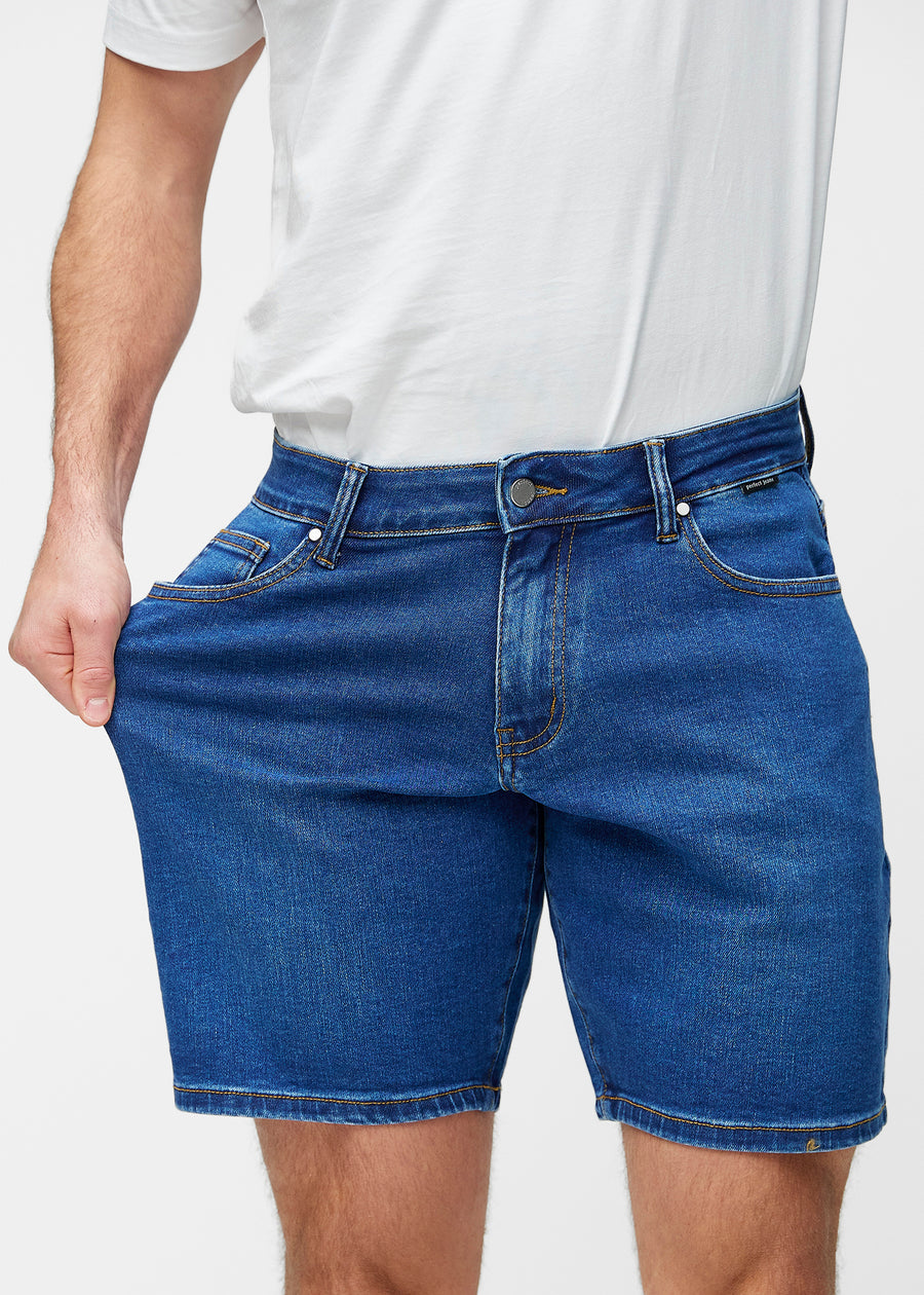 Modell strekker mørkeblå denimshorts til herre i fargen Oceans ved låret for å vise materialets stretch.
