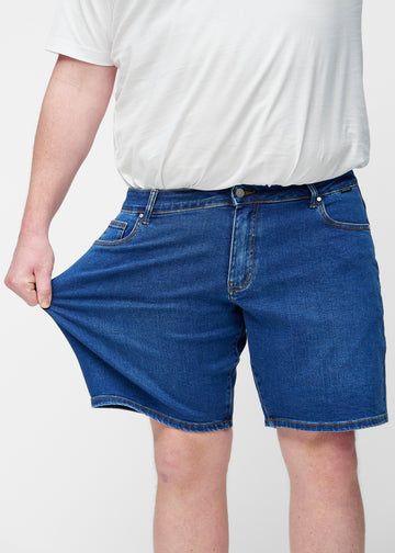Plus-size modell strekker mørkeblå denimshorts til herre i fargen Oceans ved låret for å vise materialets stretch.
