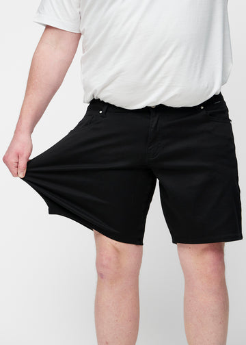 Plus-size modell strekker sorte shorts til herre i fargen Ravens ved låret for å vise materialets stretch.