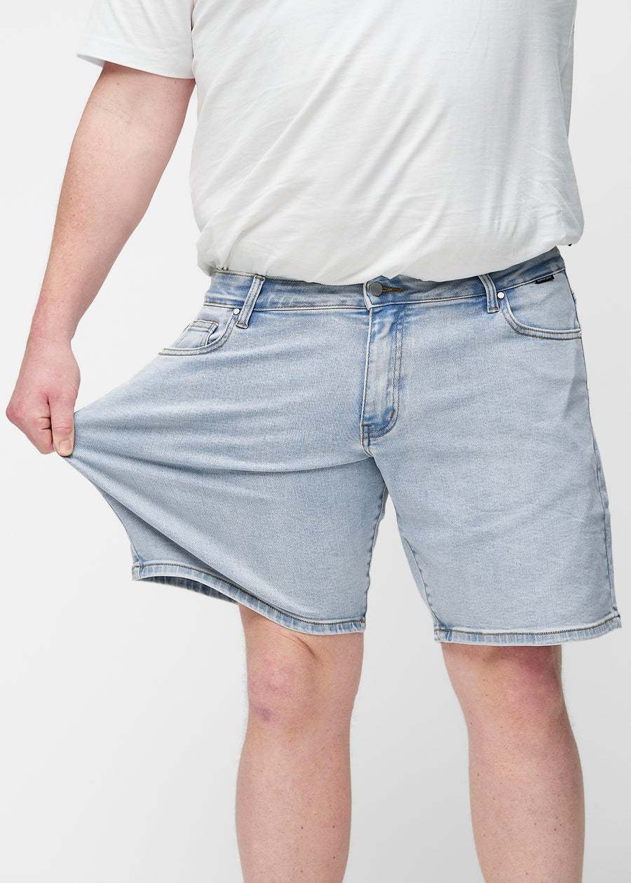 Plus-size modell strekker lyseblå denimshorts til herre i fargen Waves ved låret for å vise materialets stretch.