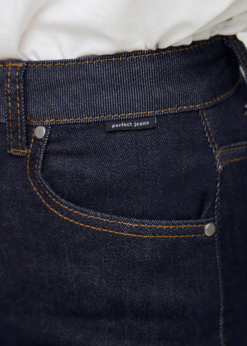 Nærbilde av dyp mørkeblå denim med Perfect Jeans logoetikett ved frontlommen.