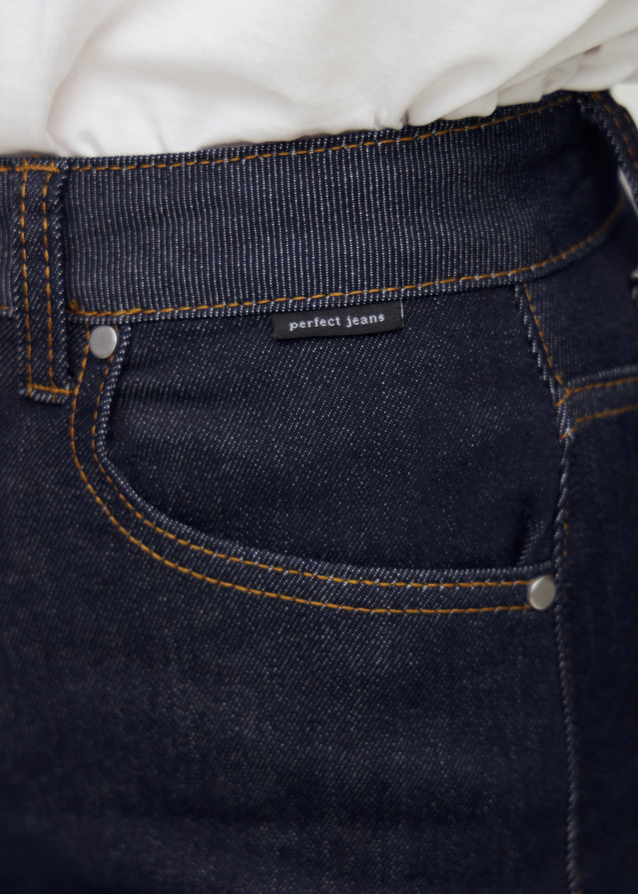 Nærbilde av dyp mørkeblå denim med Perfect Jeans logoetikett ved frontlommen.
