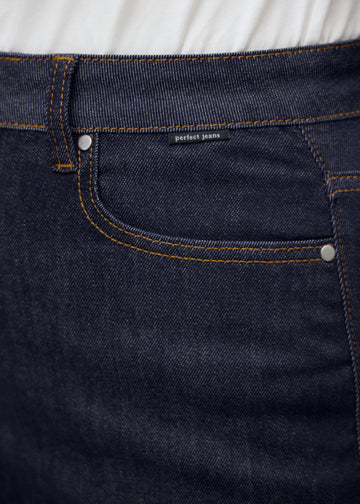 Nærbilde av dyp mørkeblå denim med Perfect Jeans logoetikett ved frontlommen på plus-size modell.