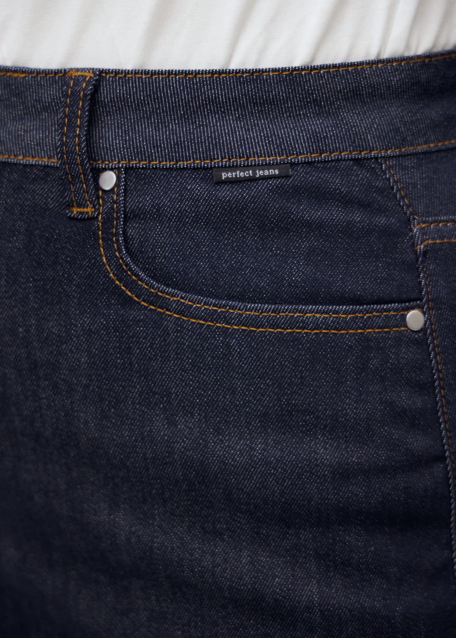 Nærbilde av dyp mørkeblå denim med Perfect Jeans logoetikett ved frontlommen på plus-size modell.