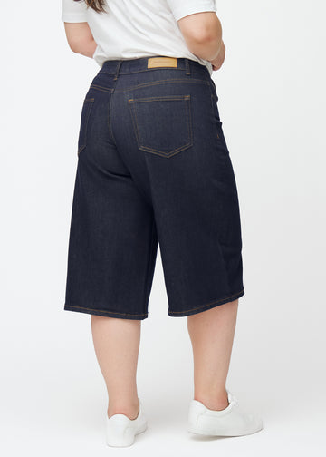 Dyp mørkeblå denim capris til dame i fargen Midnights sett bakfra på plus-size modell.