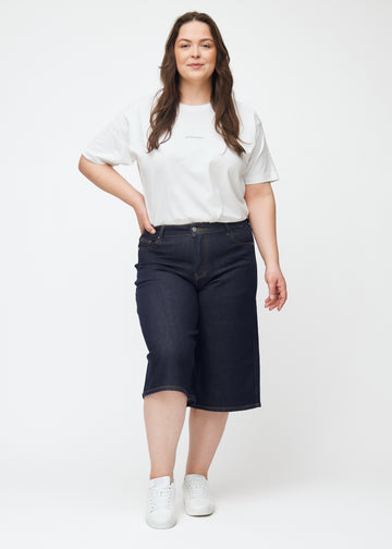 Helbilde av plus-size modell i dyp mørkeblå denim capris til dame i fargen Midnights med loose passform.