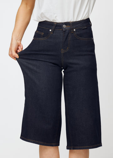 Modell strekker dyp mørkeblå denim capris til dame i fargen Midnights ved låret for å vise materialets stretch.