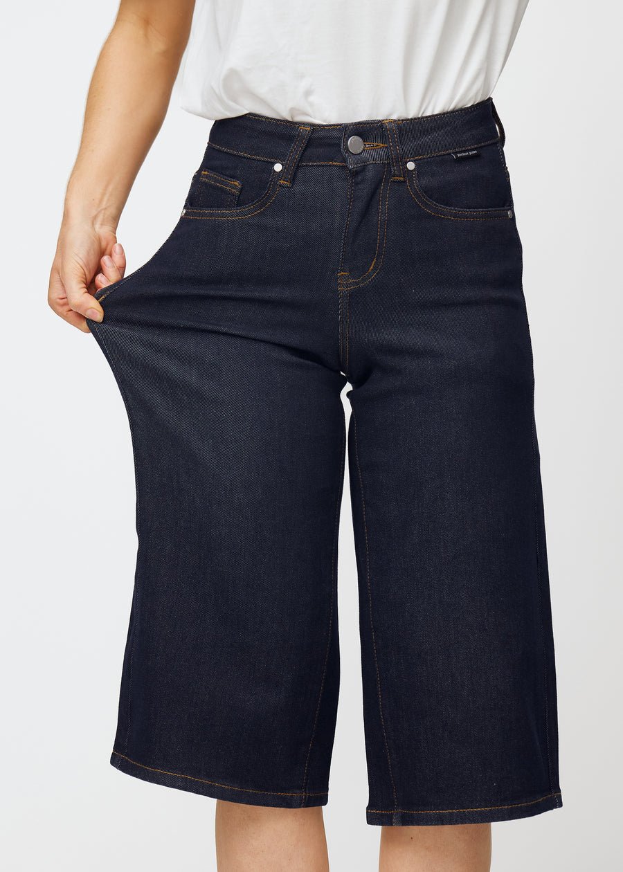 Modell strekker dyp mørkeblå denim capris til dame i fargen Midnights ved låret for å vise materialets stretch.